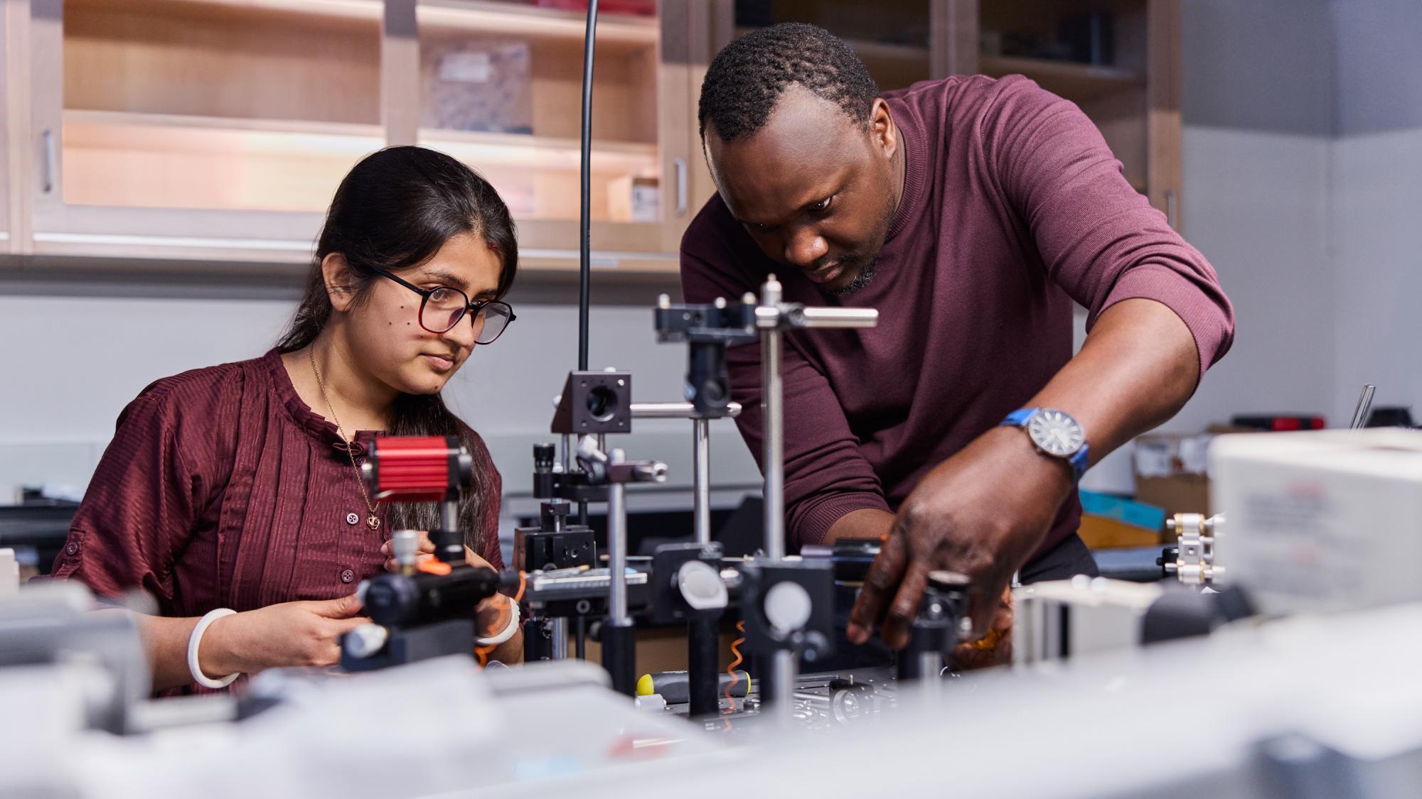 Two individuals in a laboratory setting, closely observing and adjusting complex scientific equipment with lenses and mounts.