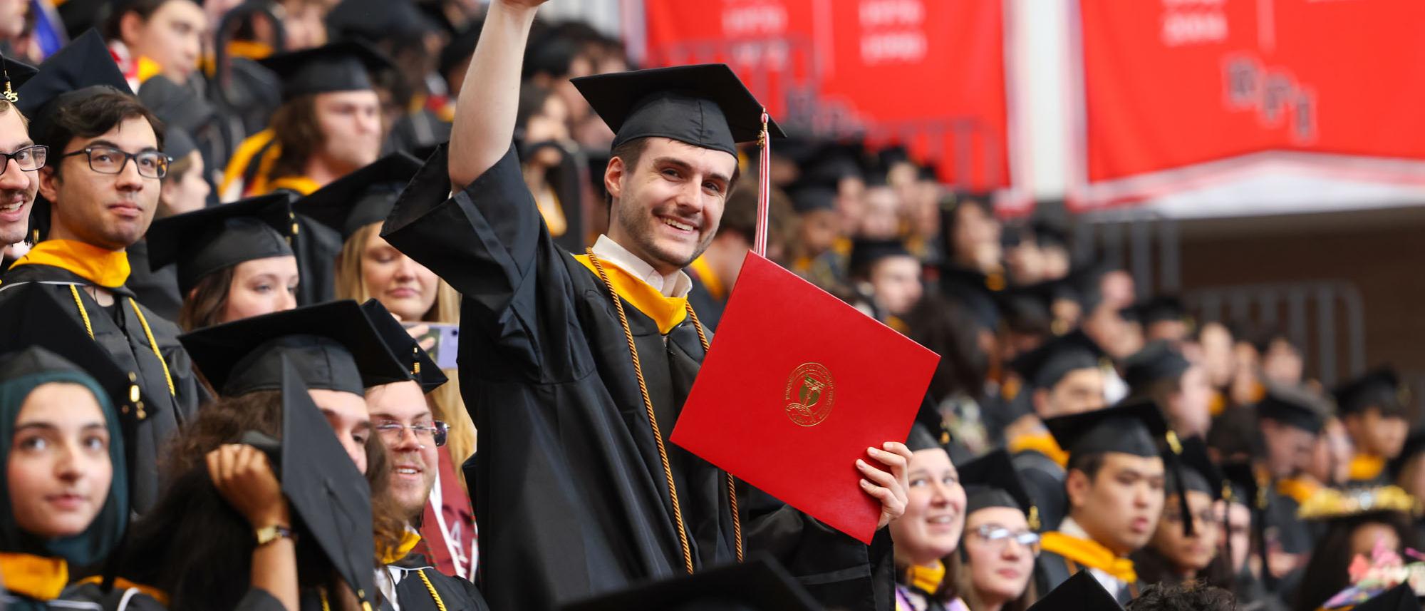 RPI Graduate stands in the crowd holding red diploma